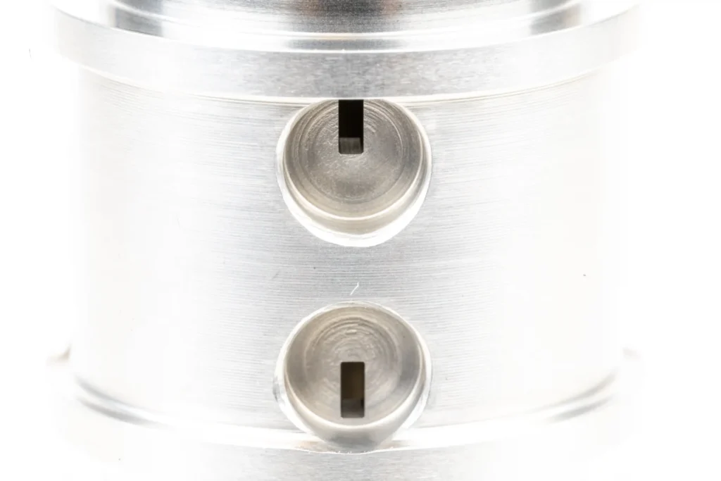 Gros plan sur une pièce cylindrique en métal, usinée de haute précision avec deux alésages micromécaniques.