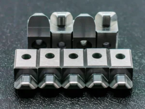 Série de microcomposants métalliques rectangulaires usinés avec perçages de précision, alignés sur table.